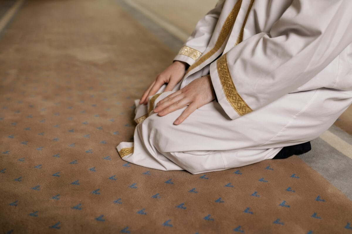 A man kneeling in prayer, wearing a traditional thawb during a religious moment.
