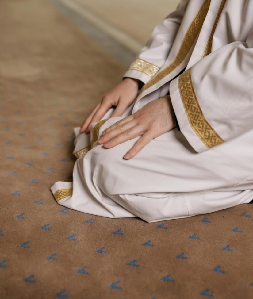 A man kneeling in prayer, wearing a traditional thawb during a religious moment.
