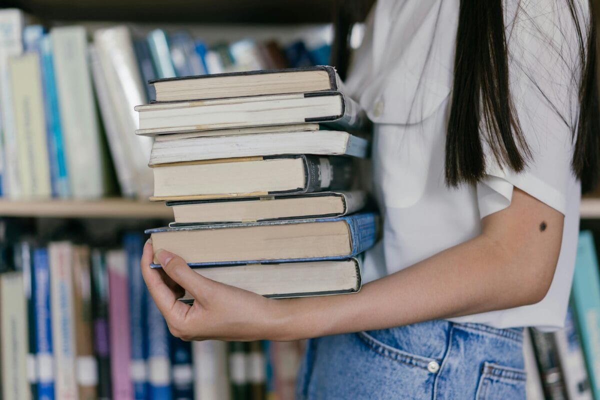 Person holding stack of books in a library. Perfect for educational themes.