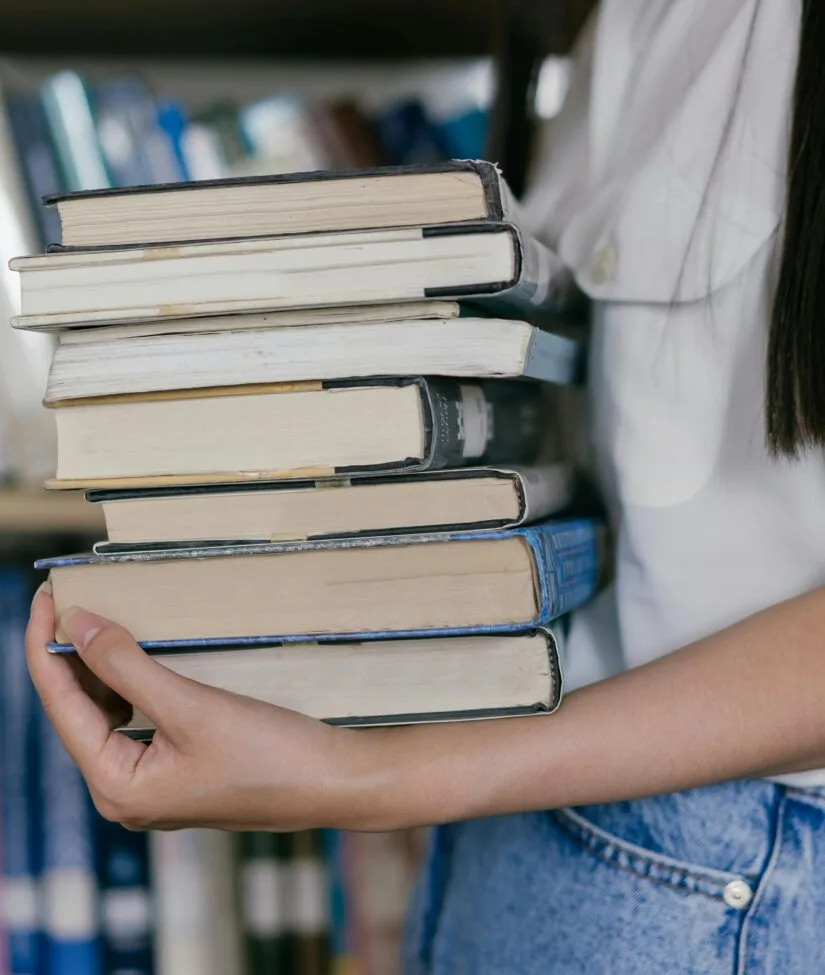 Person holding stack of books in a library. Perfect for educational themes.