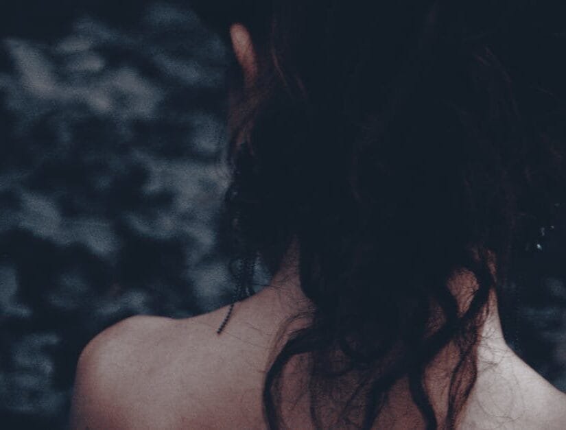 Artistic portrait of a woman seen from behind, highlighting her hair and bare shoulders in a moody setting.