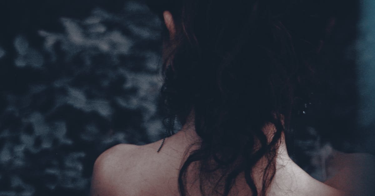 Artistic portrait of a woman seen from behind, highlighting her hair and bare shoulders in a moody setting.