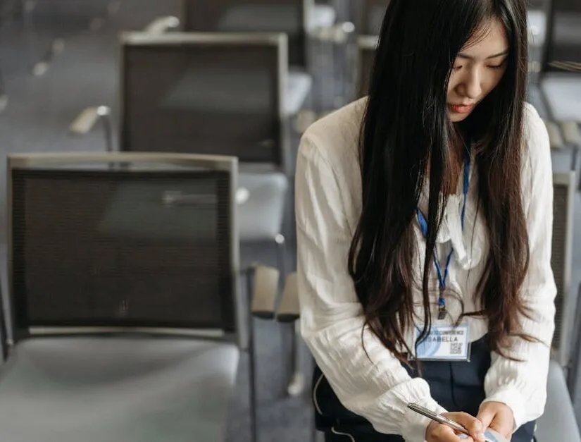 Asian woman taking notes during a seminar in an empty room with chairs.